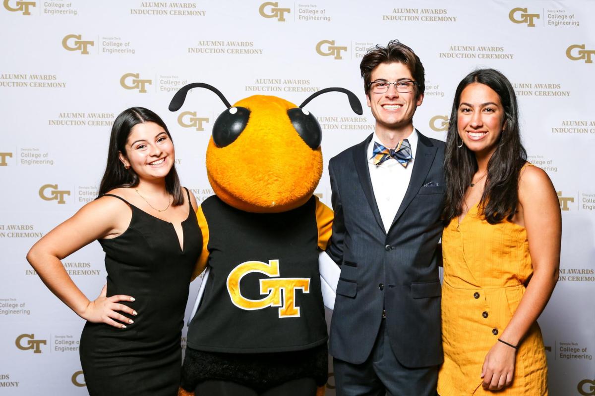 A group of students with Buzz in front of a step and repeat backdrop at the Alumni Awards